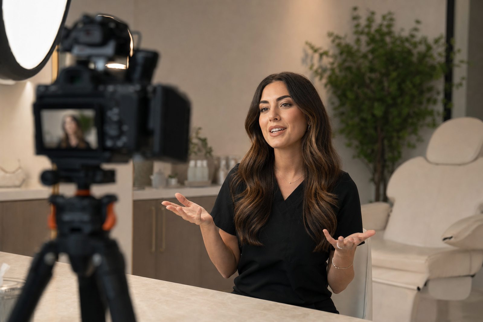 Med spa provider recording an educational treatment explainer video on camera in a clean modern aesthetic clinic, with a content idea board in the background